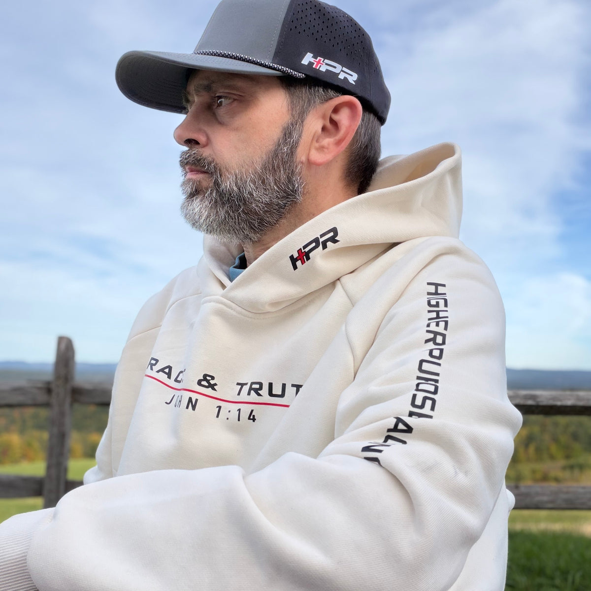 Man wearing the Vintage Pearl Team Grace & Truth hoodie outdoors by a fence