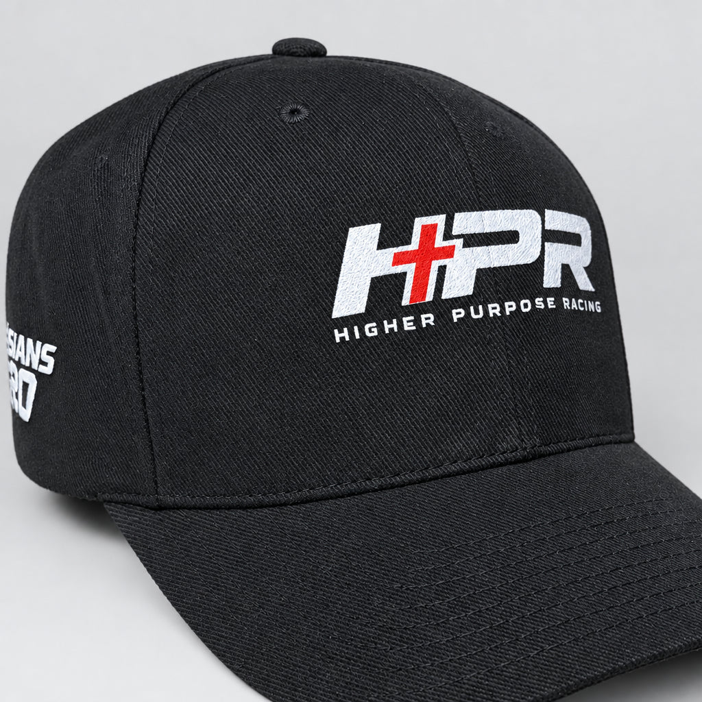 A black baseball cap with a white and red embroidered 'HPR' logo and 'HIGHER PURPOSE RACING' text on the front, resting on a wooden surface.