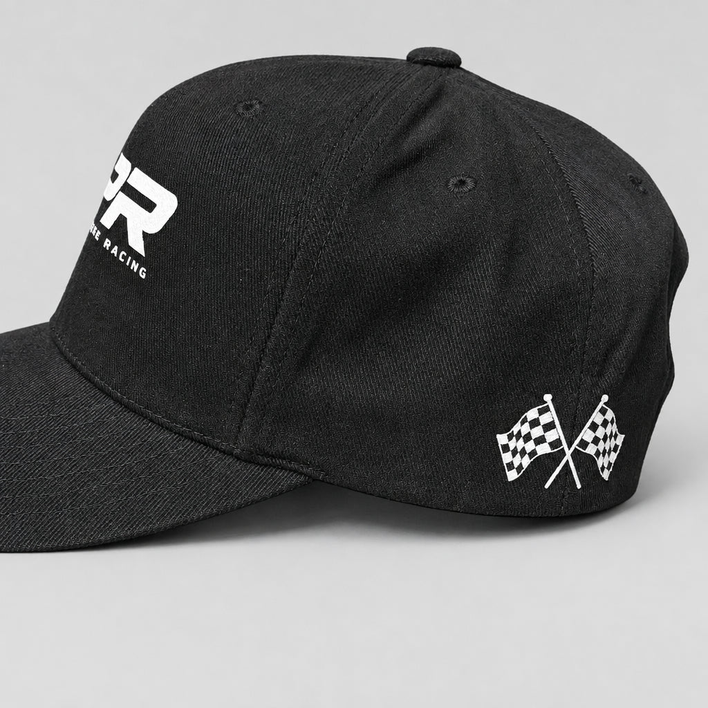 A dark gray baseball cap with a white embroidered 'Racing' logo on the front and crossed checkered flags on the side, resting on a wooden table.