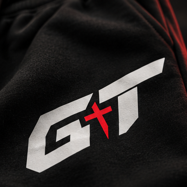 Close-up of a black hoodie or sweatshirt fabric with a large stylized white 'GT' logo and a red cross symbol on the chest, plus a black drawstring visible at the upper left.