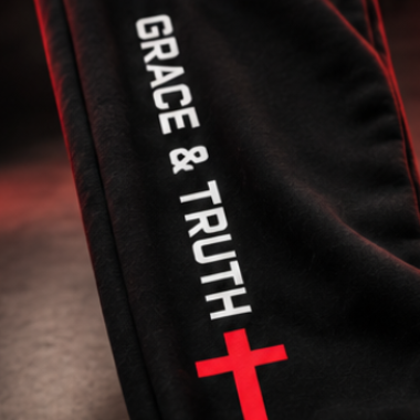 Black athletic pants with white 'GRACE & TRUTH' text and a red cross graphic on the leg, shown in a dramatic close-up with red lighting.