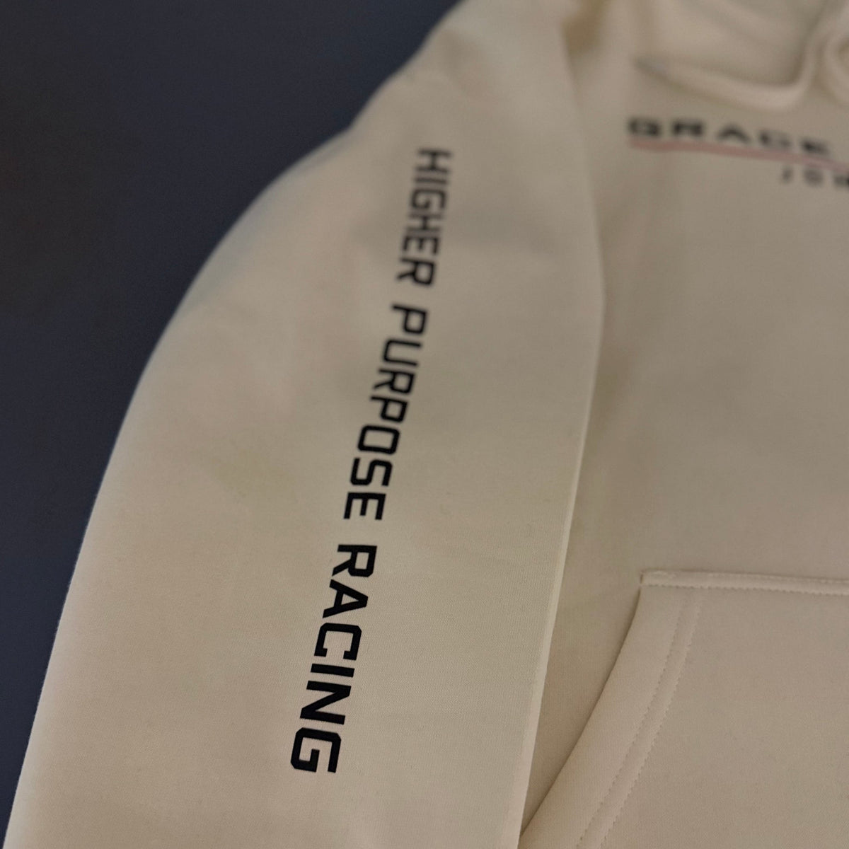 Higher Purpose Racing printed down the sleeve of the Vintage Pearl hoodie