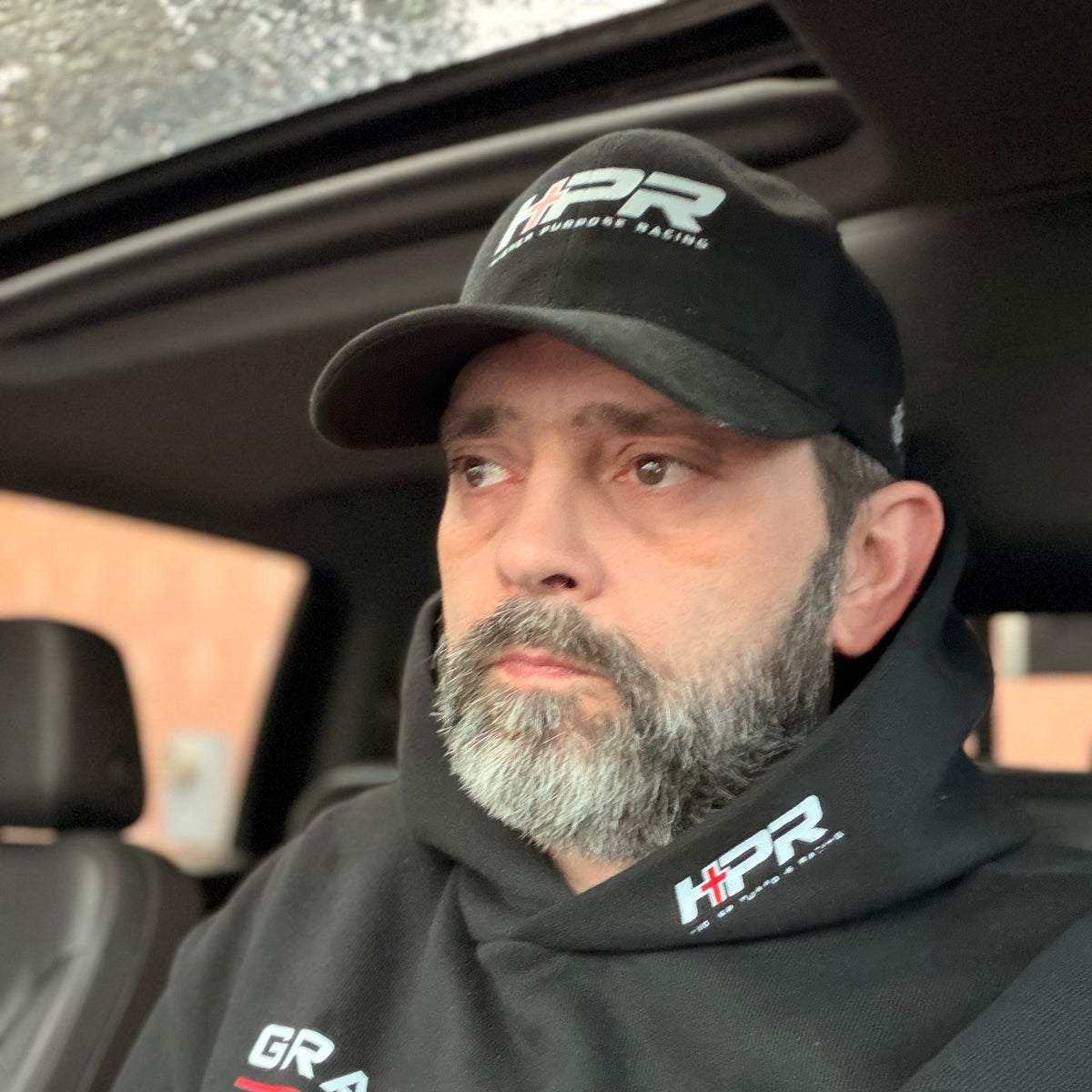 Man wearing the black Team Grace & Truth hoodie and an HPR hat in a truck